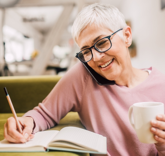 Gleitsichtbrille: Ältere Frau telefonierend mit Kaffeetasse und Stift in der Hand
