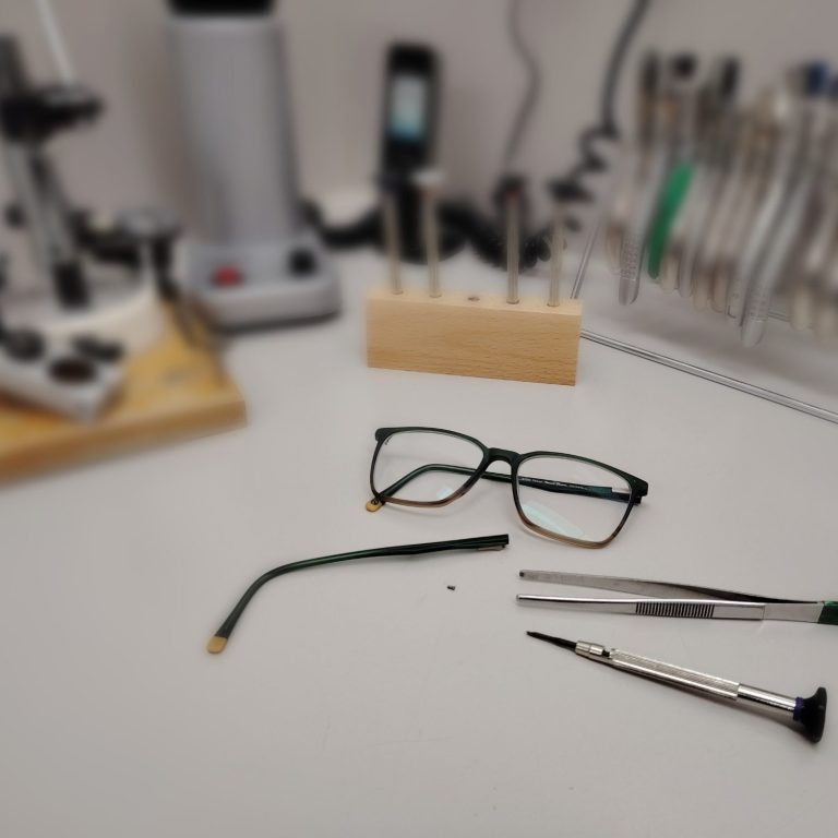 Brille, Schraubendreher und Werkzeuge auf einem Tisch in einer Werkstatt.